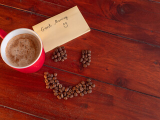 Red coffee mug with Good Morning sticky note and coffee bean smiley face on rustic wood