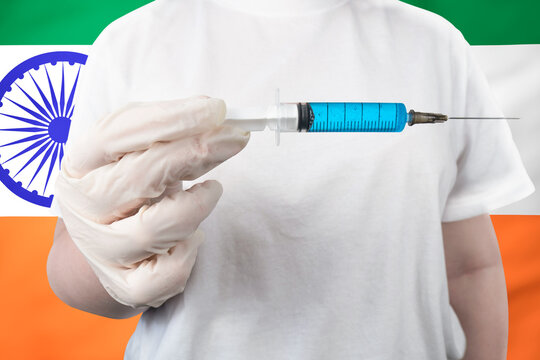 A hand in a white medical glove holds a syringe with blue vaccine against the background of the Indian flag. Healthcare and medicine in India - Powered by Adobe