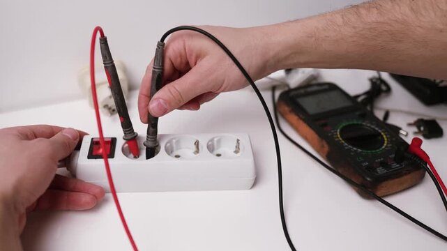 Close up on hands of caucasian man electrician using multimeter working on the plug electric or extension power strip, electric socket.