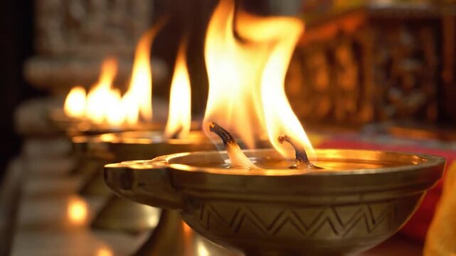 Lit golden oil lamps glow warmly in a soft-focus setting, casting a devotional light