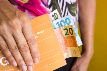 Guia de pagamento da previdência Social GPS brasileiro com idosa segurando cédulas de dinheiro...