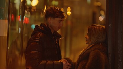 A young couple holds hands in a romantic urban scene in Paris at night with bokeh lights adding to...