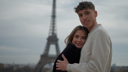 A young couple is embracing in Paris France with the Eiffel Tower in the background. This image is...