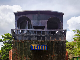 Old rusty black steam locomotive front view under a bright cloudy sky