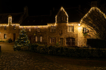Fa&ccedil;ades en pierre du village de Locronan en Bretagne illumin&eacute;es pour No&euml;l, d&eacute;corations lumineuses et ambiance nocturne calme dans un village breton authentique.