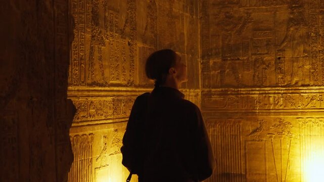 A female tourist admires the interior of the temple in Dendera or the temple of Hathor in Egypt. Ancient hieroglyphic carvings on the temple walls. The history of Egypt.