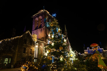 &Eacute;glise du village de Locronan en Bretagne illumin&eacute;e pour les f&ecirc;tes de No&euml;l, sapin d&eacute;cor&eacute; et d&eacute;corations lumineuses cr&eacute;ant une ambiance nocturne chaleureuse et festive.