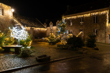 Place du village de Locronan en Bretagne illumin&eacute;e pour les f&ecirc;tes de No&euml;l, d&eacute;corations lumineuses et fa&ccedil;ades en pierre cr&eacute;ant une ambiance nocturne festive et authentique.