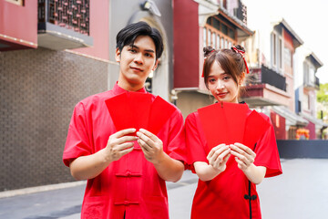 Asian man and woman proudly display bright red envelopes while wearing stylish cheongsam attire. They celebrate Chinese New Year together in a cheerful atmosphere, Female and Male show Ang Pao