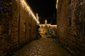 Rue calme du village de Locronan en Bretagne illumin&eacute;e pour les f&ecirc;tes de No&euml;l, d&eacute;corations lumineuses et fa&ccedil;ades en pierre cr&eacute;ant une ambiance nocturne douce et chaleureuse.