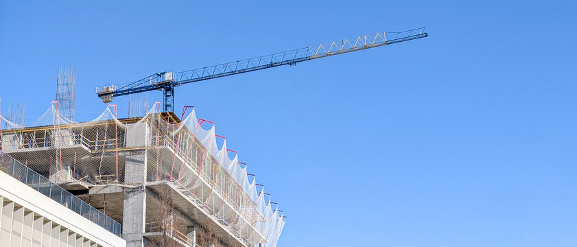 Building construction site with tower crane extending into clear blue sky, concrete structure under development, modern architecture expanding urban skyline, progress and infrastructure growth