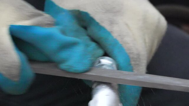 Metalworking filing workshop. Worker uses a rasp file tool to grind the sharp edges off a piece of metal tubing during industrial maintenance.