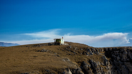 A small structure sits atop a rocky hill under a clear blue sky