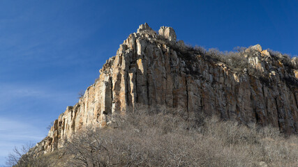 Rocky cliff with sparse vegetation under clear blue sky © Михаил Уванов
