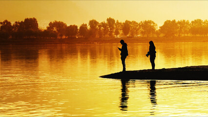Two People Standing On Pier At Sunset