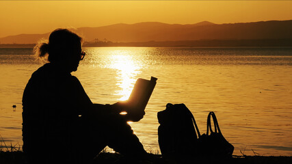 Woman Watching Sunset And Reading Book By The Sea