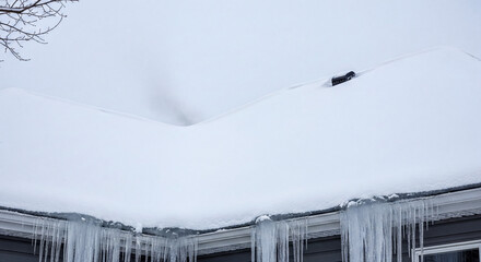 Heavy snow and icicles on a residential roof.
A thick layer of white snow covers a house roof with long, sharp icicles hanging from the gutters during a cold winter day