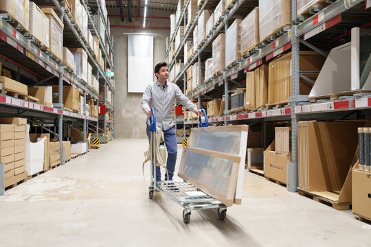 Man pushing cart with furniture in warehouse aisle. shopping, renovation, DIY