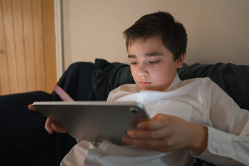 Young student read e-book on digital tablet computer at home. Teen kid wearing white school shirt doing homework concept modern online learning, digital literacy, and remote education for children