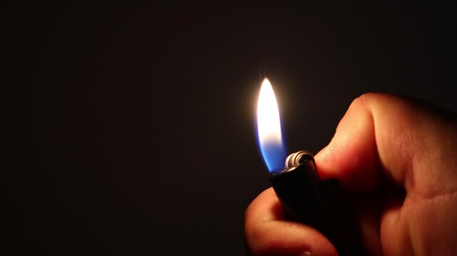 Close up shot of a lighter being ignited in complete darkness. Bright flame illuminating the scene. Concept of fire, energy, ignition, danger, survival, mystery and minimal lighting.