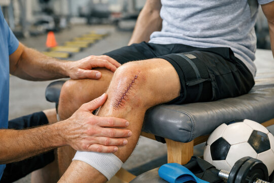 Rehabilitation healing recovery knee physical therapy injury Patient undergoing rehab after surgical knee incision; therapist palpating scar and guiding movement with calm care