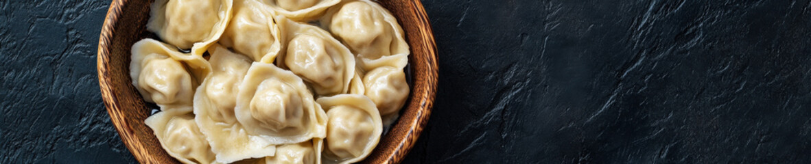 Boiled dumplings in wooden bowl on dark stone background, top view


