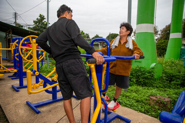 Senior woman using outdoor exercise equipment with support from her partner, highlighting active...