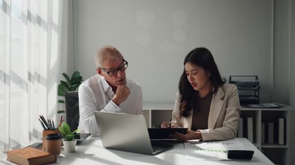 Young asian businesswoman explaining a project on a tablet to her thoughtful senior caucasian boss during a meeting in a modern office