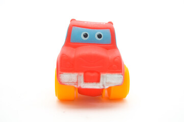 Fototapeta premium Cute red toy car with large yellow wheels and a smiling face isolated on white background. Fun plastic vehicle for kids play, early education, and creative design.