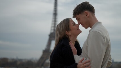 A romantic couple embraces in Paris France with the Eiffel Tower in the background. This image is...