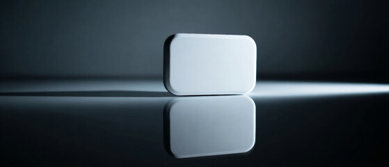 A white, rectangular bar of soap is balanced on its edge with a reflection below it in this dark image