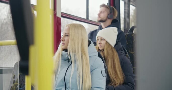 Side view of passengers going home by bus. Blonde woman sitting, young girl in white hat looking in window, boy with earphones listening to music. Concept of public transport.