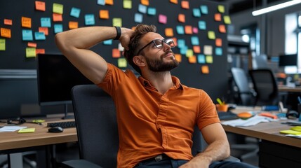 A man in an orange shirt is sitting in a chair with his head on his hand