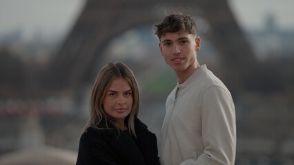 A young couple poses in Paris France with the Eiffel Tower in the background. This image is suitable for travel and tourism advertising Valentine's Day concepts and relationship themes. © 4kclips