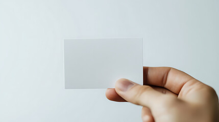 Close-up of a hand holding a blank, white card. The background is a clean, light gray. Minimalist design. The card is crisp, and the hand's grip is gentle and precise.