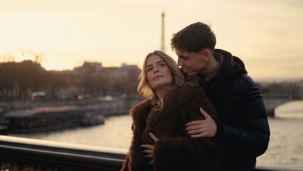 A romantic couple embraces on a bridge in Paris France with the Eiffel Tower visible in the...