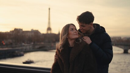 A romantic couple embraces with the Eiffel Tower in the background in Paris France at sunset. This image can be used for travel Valentine's Day or honeymoon concepts.