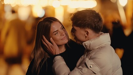 Fototapeta premium A romantic couple embraces in Paris at night surrounded by bokeh lights The young woman and man are in love enjoying a city break and European vacation.