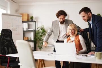 Three team members work together at a table in an office. They discuss ideas while looking at a laptop screen and share thoughts on a project during a brainstorming session.