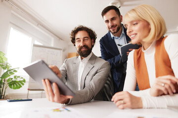 Group of professionals collaborates and shares ideas on a tablet in a bright office space. They focus on brainstorming to achieve business success.