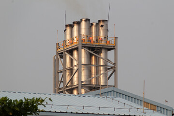 Multiple industrial stainless steel chimneys stacked together emitting minor smoke against a grey overcast sky.