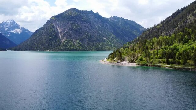 Aerial view of a winding road along the turquoise Lake Plansee in the Tyrolean Alps, Austria.