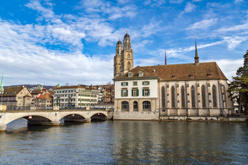 Obraz premium Scenic view of the historic Grossmunster church and Wasserkirche on the banks of the Limmat river with the Munsterbrucke bridge under a bright blue sky in Zurich, Switzerland