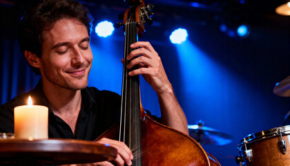 Fototapeta premium A young Caucasian man with curly hair plays a double bass on stage. Soft blue lights illuminate the scene, creating a cozy jazz atmosphere.