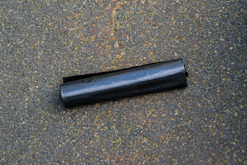 Black roll of garbage bag for bulky waste on asphalt ground. Large refuse sack for trash disposal and cleanup. heavy duty 120 liter bags