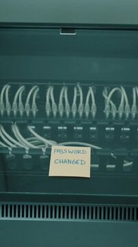 Hand Placing "Password Changed" Sticky Note on Data Center Server Rack, System Maintenance: "Password Changed" Note Placed on Server Hardware