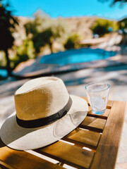 Straw hat with empty glass on wooden table by a pool during summer.