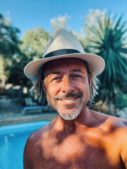 Happy blond man with straw hat and a stubble beard by a pool in a sunny summer garden.