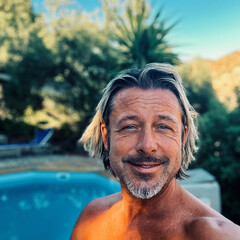 Happy blond man with a stubble beard by a pool in a sunny summer garden.