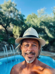 Happy blond man with straw hat and a stubble beard by a pool in a sunny summer garden.